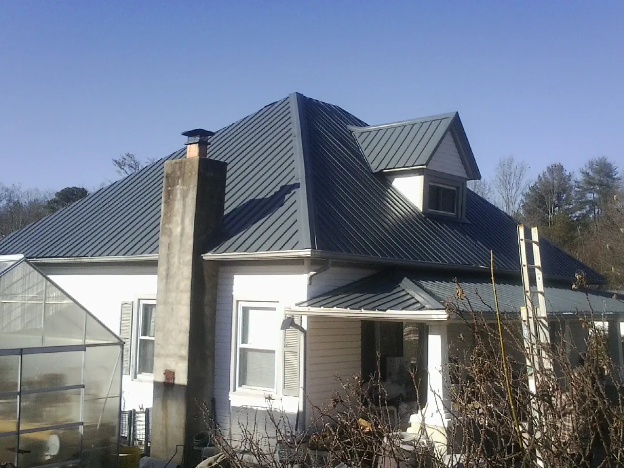 Dark blue standing seam metal roof on a white farmhouse with dormer — Slate & Tile Roof Repair by Roofing Brothers in Russell
