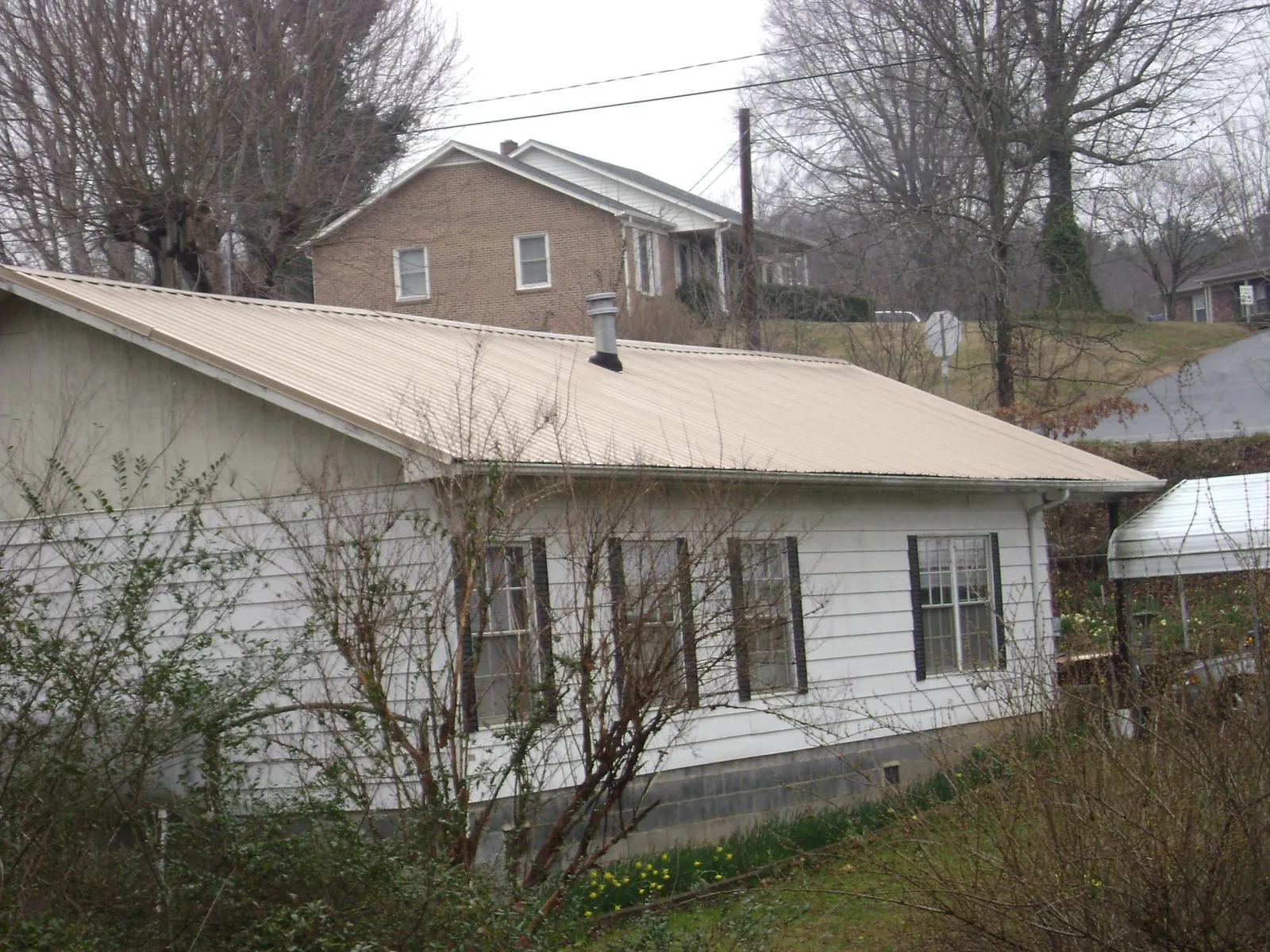 Tan metal roof on a white sided house set into a hillside — Commercial Roofing by Roofing Brothers in Russell