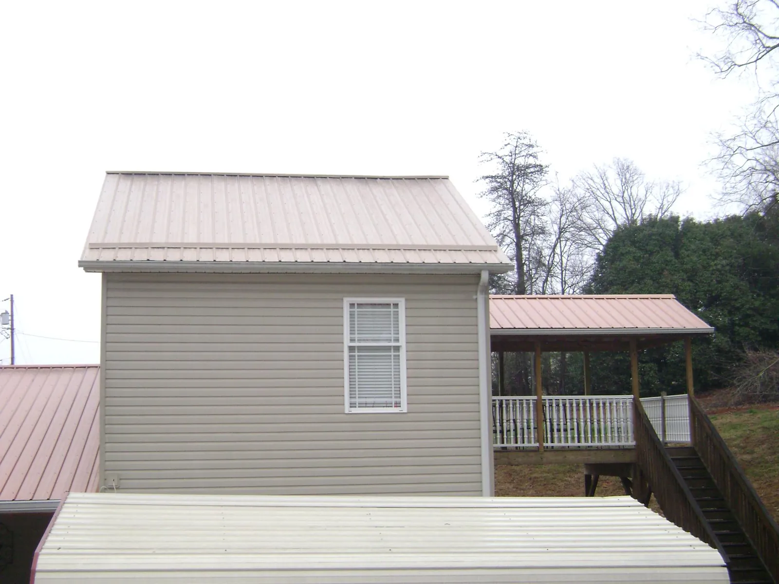 Tan metal roofs on a two story addition and attached porch, from a Roof Replacement job in Russell